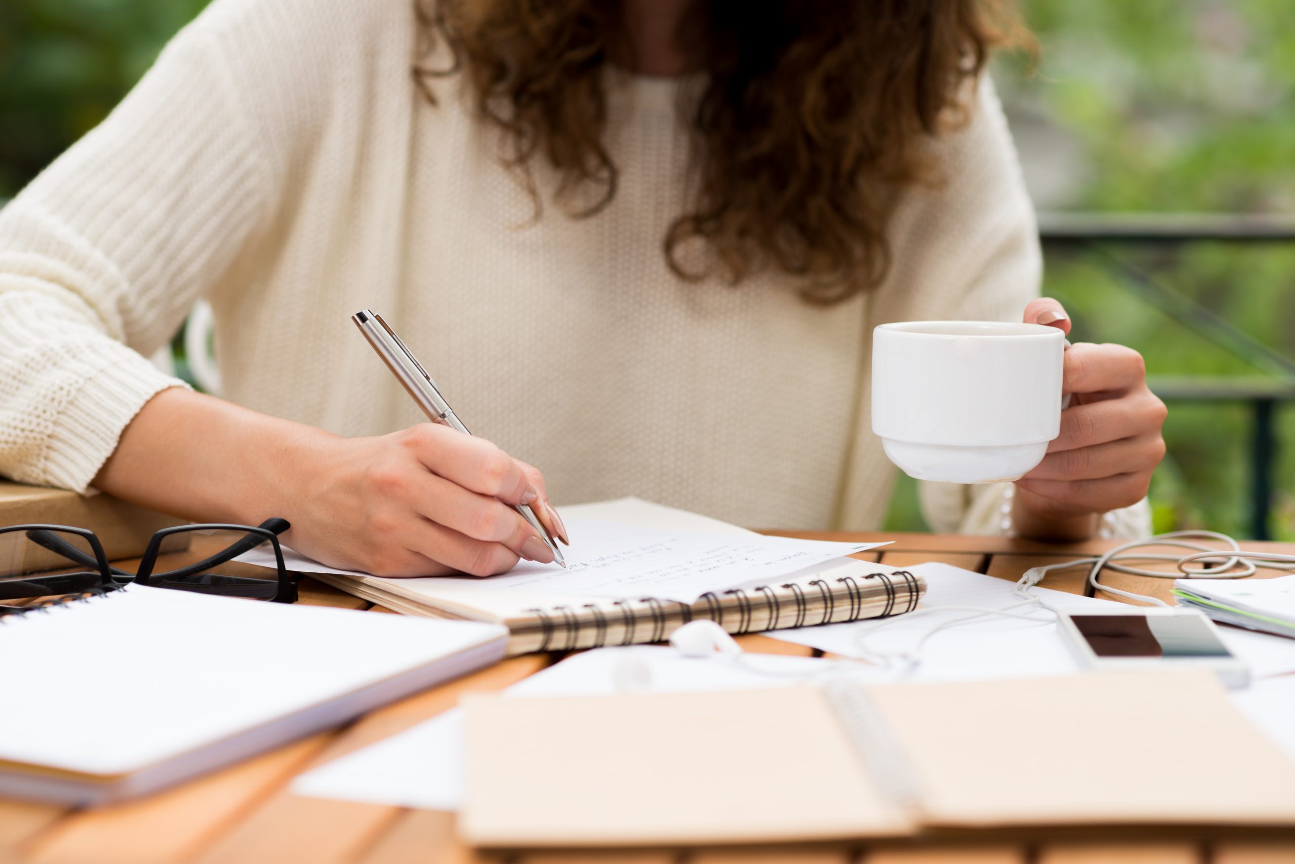 Cropped image of female university student drinking coffee and writing an essay in outdoor cafe